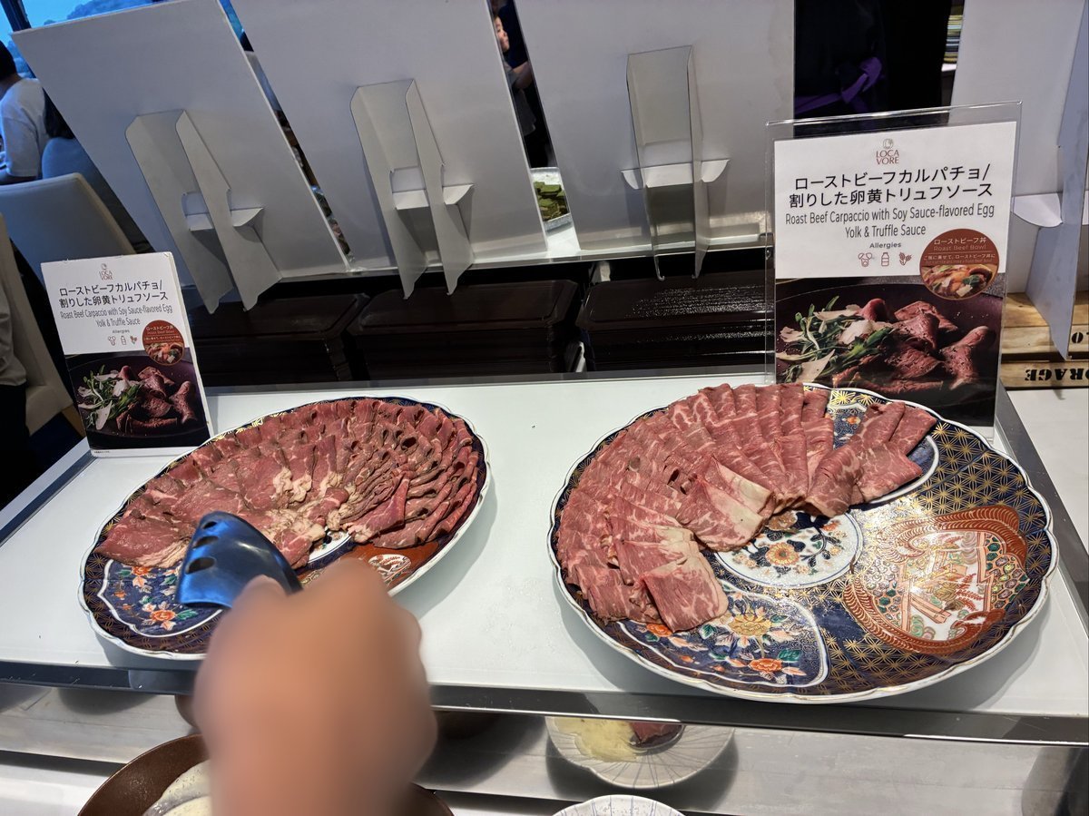 「ローストビーフカルパッチョ」の案内板が立つ料理台。薄くスライスされたローストビーフが、華やかな絵柄の大皿にたっぷりと盛り付けられている。