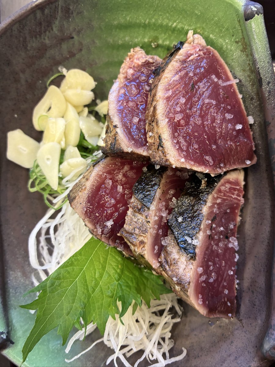 藁焼きで香ばしく炙られたカツオのたたき。厚切りにされた身には粗塩が輝き、薬味のニンニクや大葉が添えられ、食欲をそそる一品。