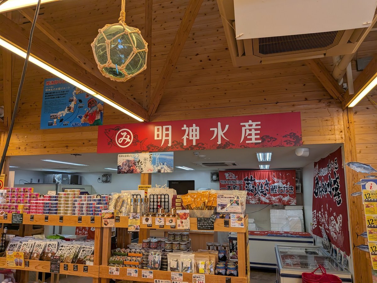 「明神水産」の大きな赤い看板が掲げられた直販所コーナー。新鮮な魚介加工品や地元の名産品が豊富に並び、お土産選びに最適な活気ある空間。