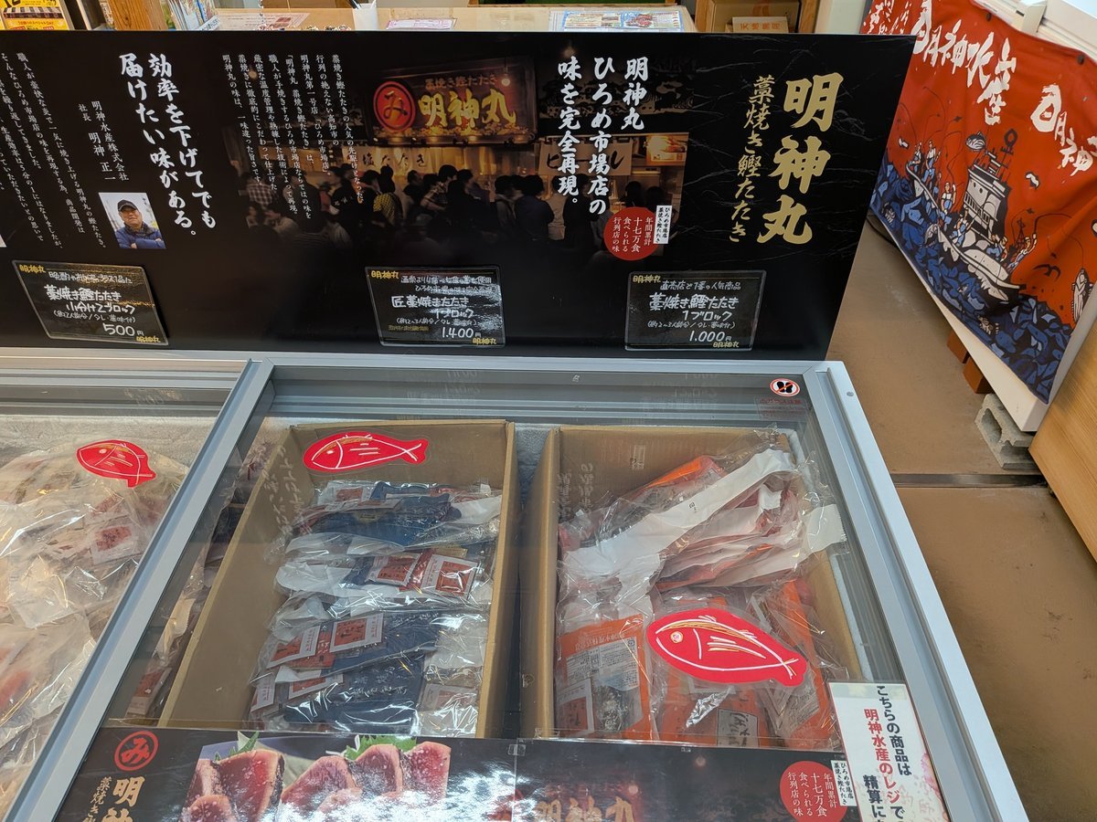 「明神丸 藁焼きたたき」の大きなポスターが目を引く冷凍カツオ販売コーナー。新鮮なカツオのたたきが真空パックで並び、自宅でも本格的な味が楽しめる。