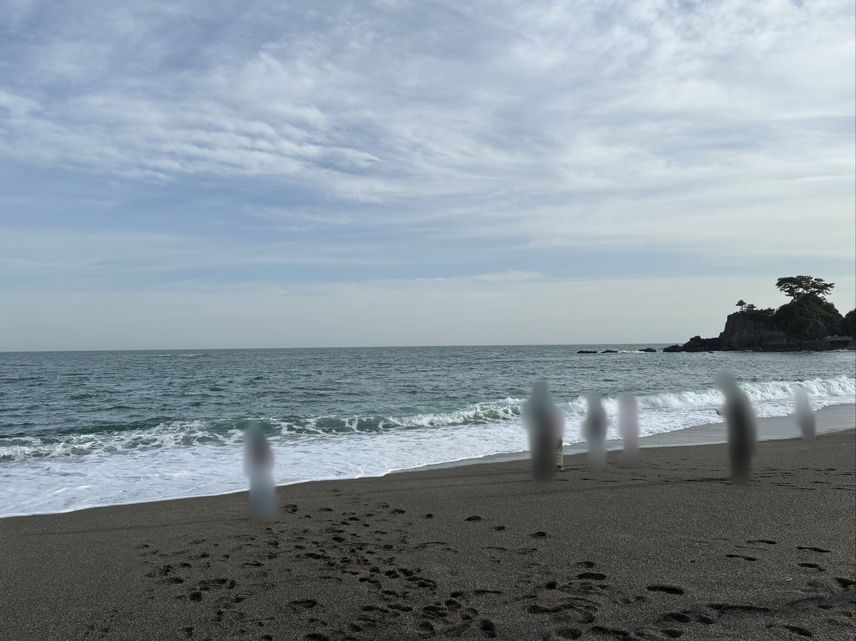 桂浜の広々とした砂浜に打ち寄せる波と、遠くに見える小さな岩島。空には白い雲が広がり、開放的な海岸の風景。