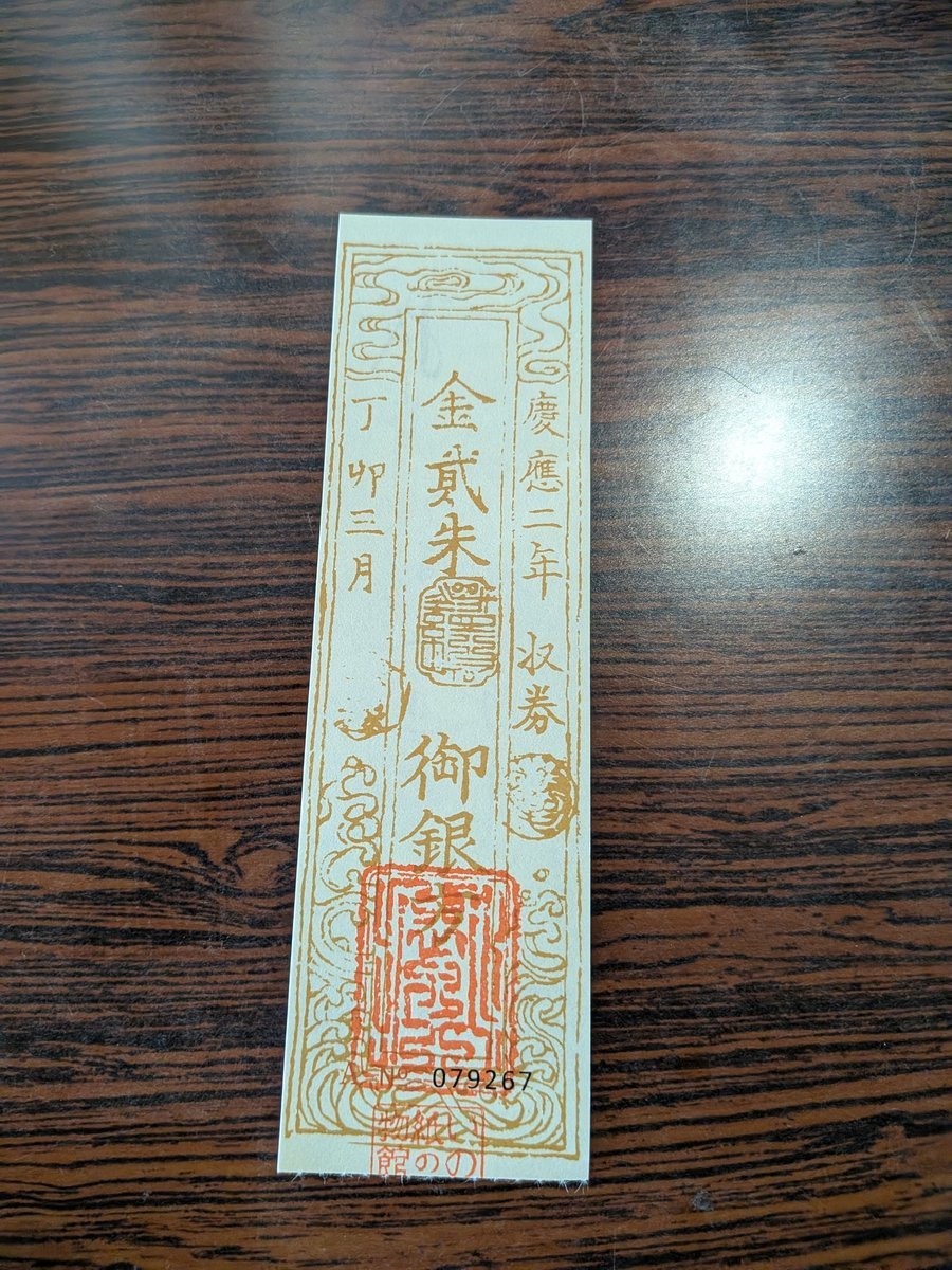 木目調のテーブルに置かれた、金弐朱や御銀の文字が書かれた昔の紙幣のようなデザインの紙片。細やかな模様が施されている。