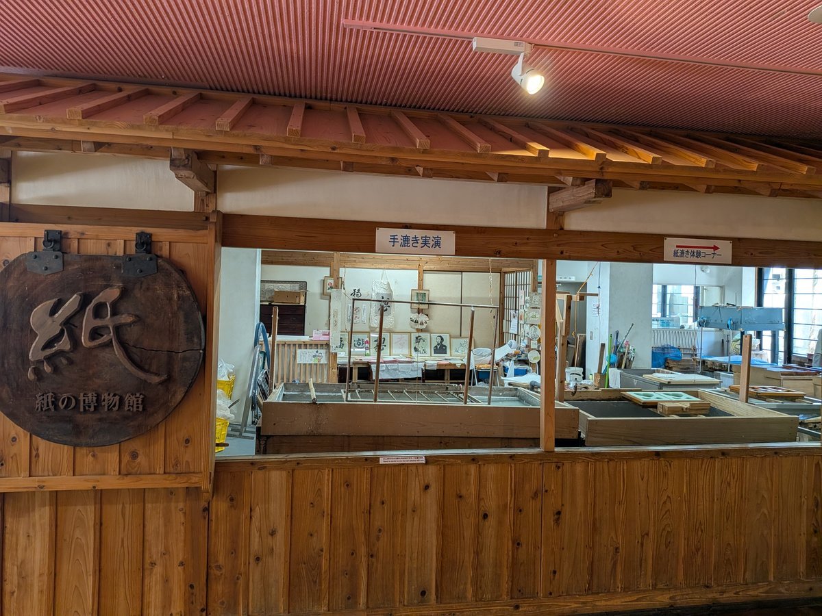 木の温もりが感じられる館内。赤い天井と木製の梁が特徴的な空間で、奥には紙漉き体験ができる大きな水槽が見える。