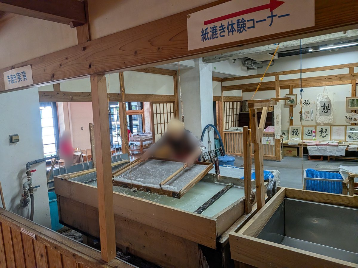 紙漉き体験コーナーの様子。水槽の中で、枠を使って紙の原料をすくい上げる作業が行われている。