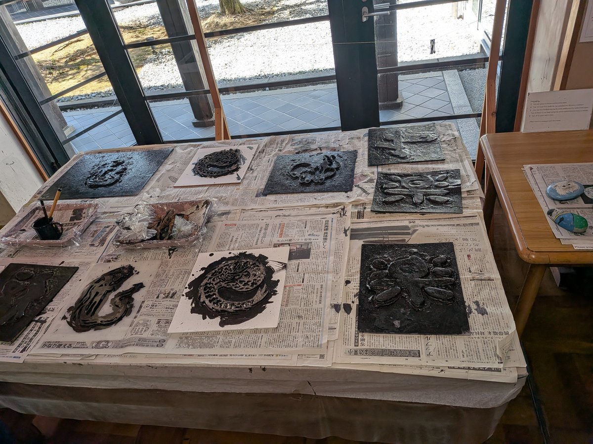 新聞紙が敷かれたテーブルの上に、黒いインクで様々な模様が描かれた版画のような作品が複数並べられている。
