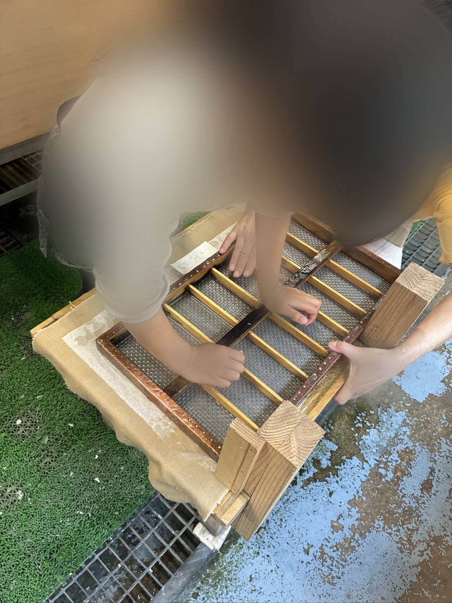 紙漉き体験の様子を上から捉えた写真。水槽の中で、網状の枠を使って紙の繊維を整えている手元が写っている。