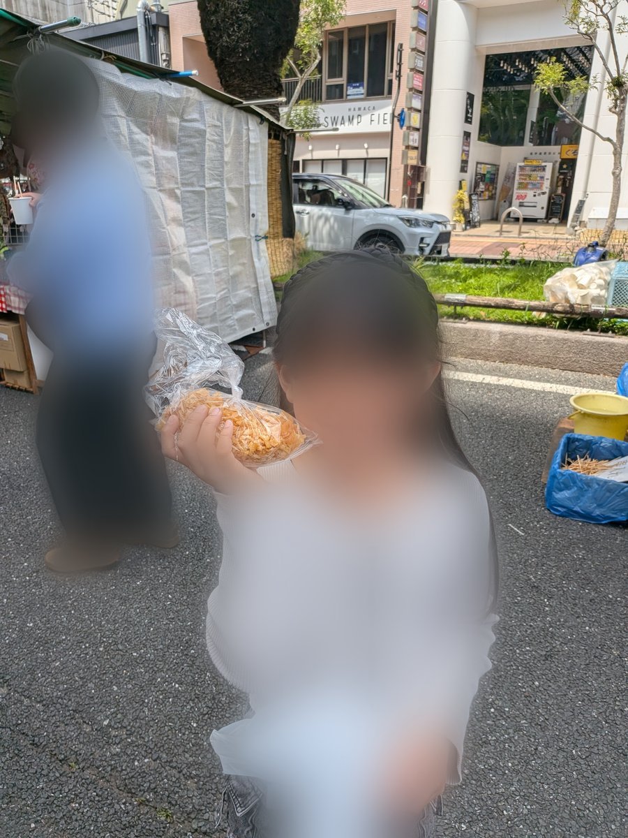 屋台で買ったばかりの「いも天」が入った袋を手に持ち、食べ歩きを楽しむ様子。