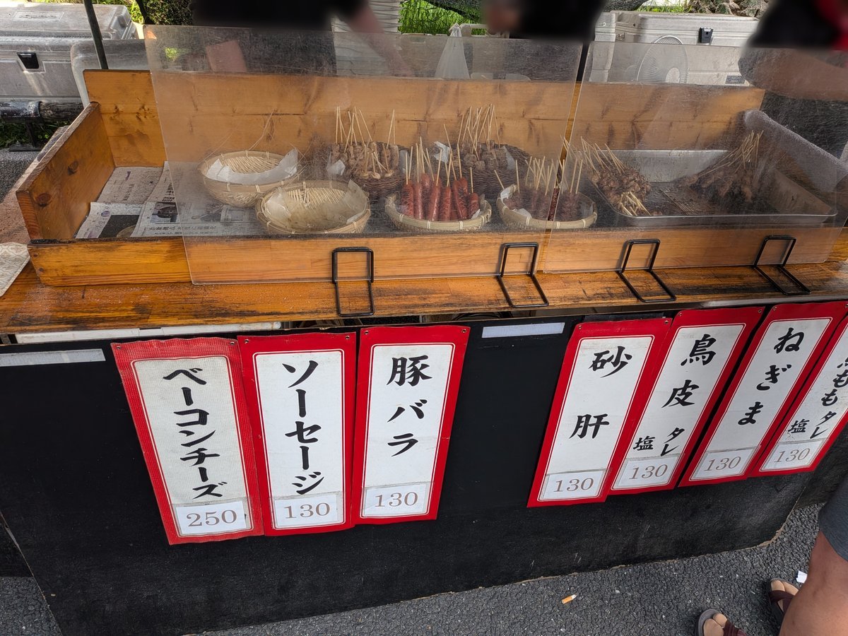 焼き鳥屋台のメニューと価格が書かれた札。「豚バラ」「砂肝」「鳥皮」など。