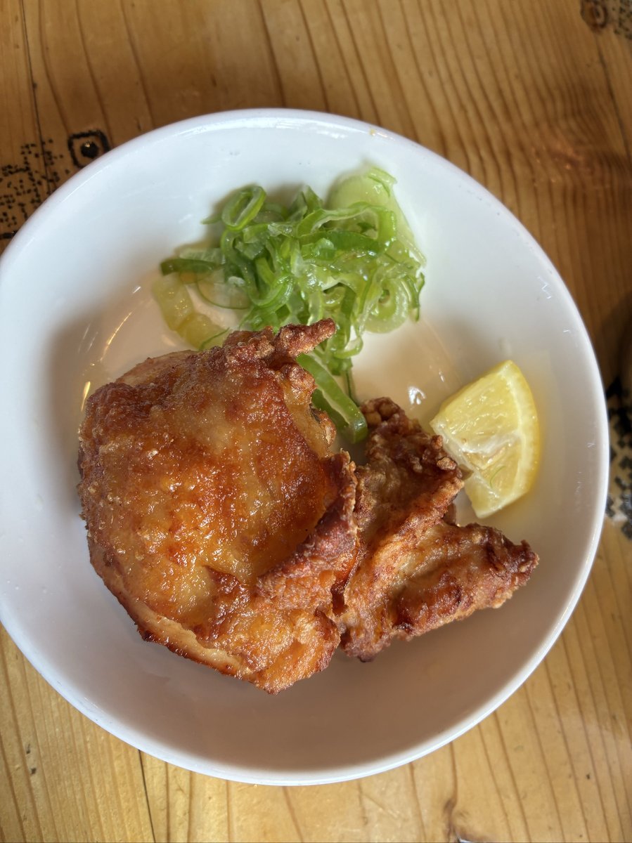 白い小皿に盛り付けられた鶏の唐揚げ。こんがりと揚がった大きな唐揚げが2個、刻みネギとレモンのくし切りが添えられている。