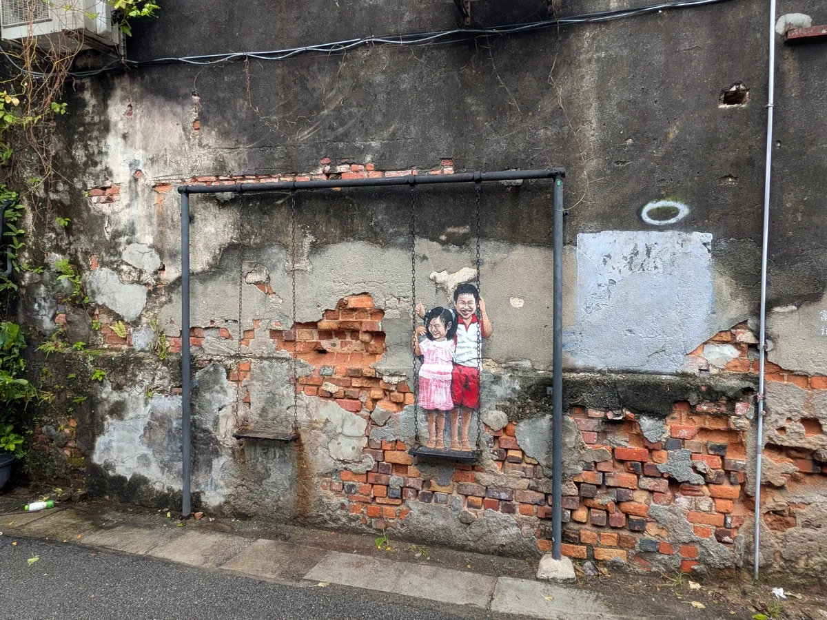 レンガがむき出しの壁に描かれた2人の子どもと、実際に座れる本物の鉄のブランコ