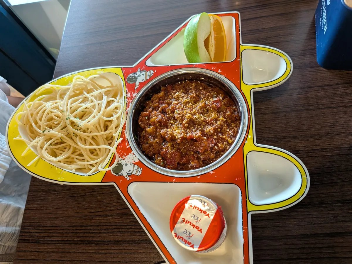飛行機の形をしたキッズプレート。スパゲッティ・ボロネーゼ、りんごとオレンジのスライス、ヤクルトが乗っている