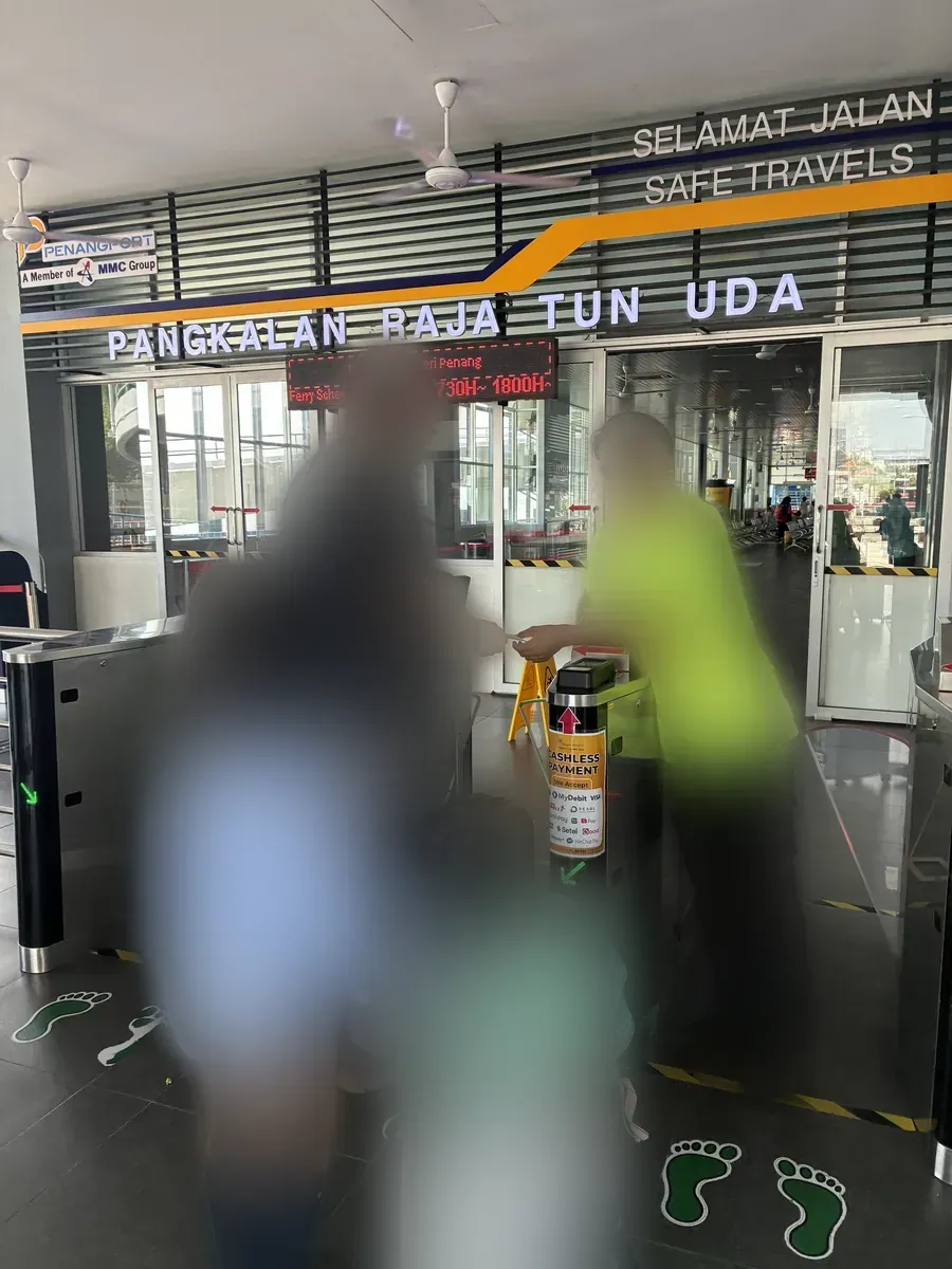 PANGKALAN RAJA TUN UDAの表示の下にある改札。乗客が荷物を持って通過する