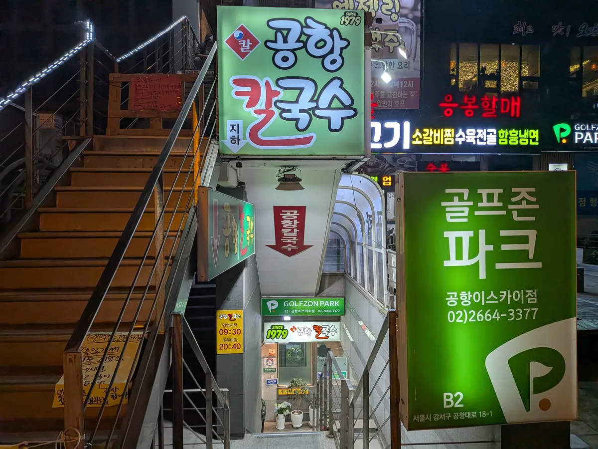 地下へ降りる階段と「공항 칼국수（地下）」の案内看板（夜）