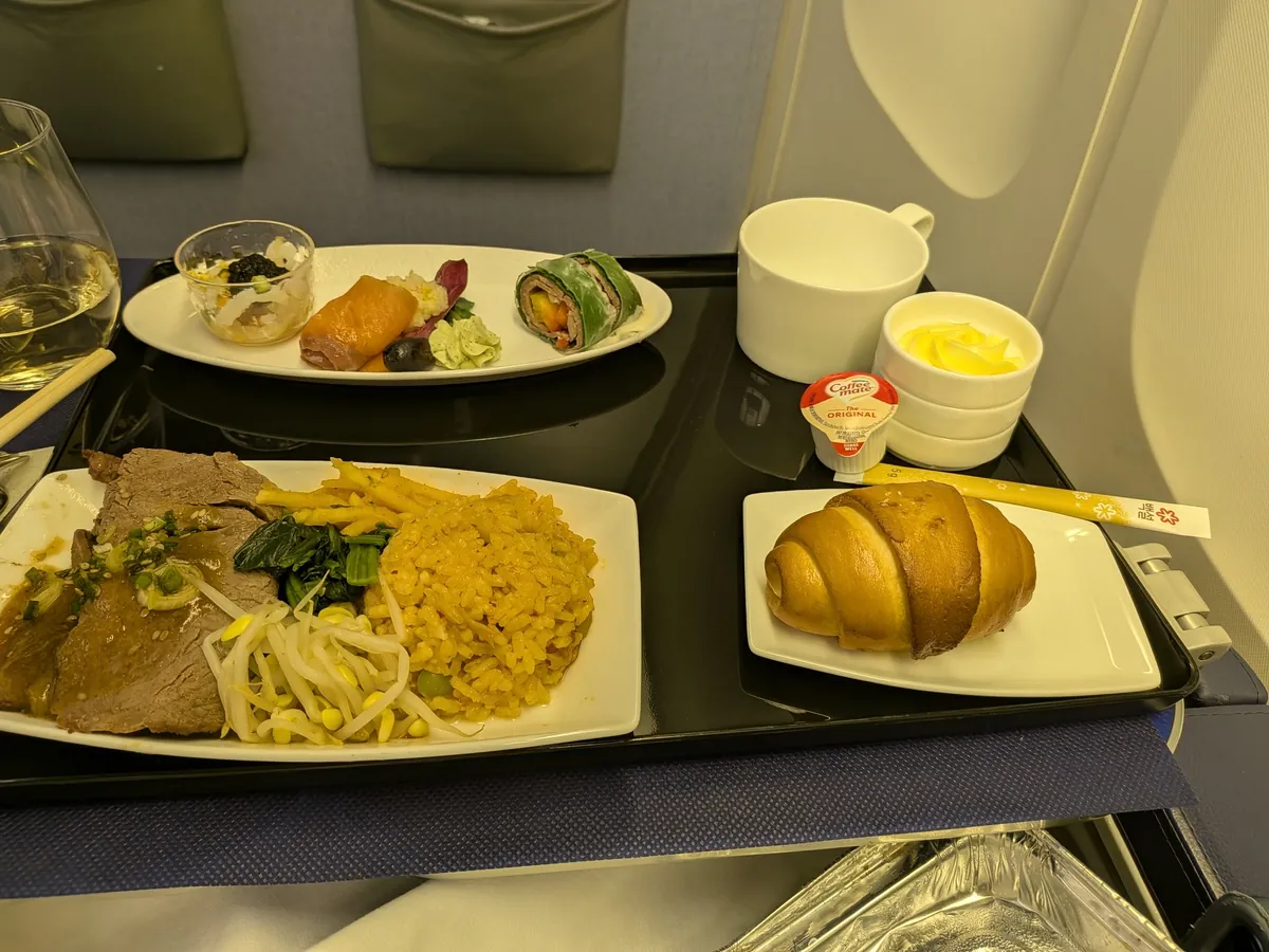 ANAビジネスクラスの機内食の全景。皿盛りの前菜とメイン、クロワッサン、コーヒー、白ワイン