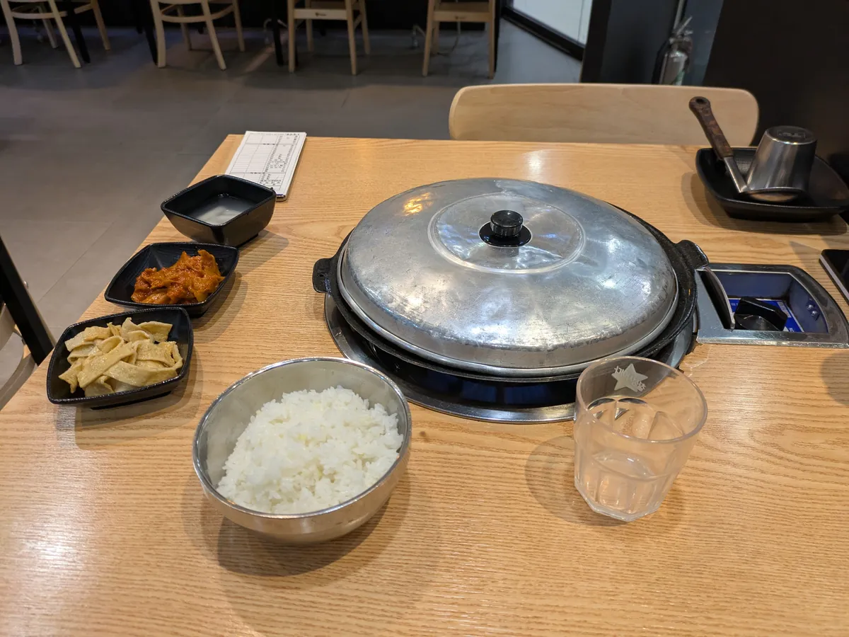 一人席にセットされた部隊チゲ。蓋つきの鍋、ご飯、キムチなどのおかず
