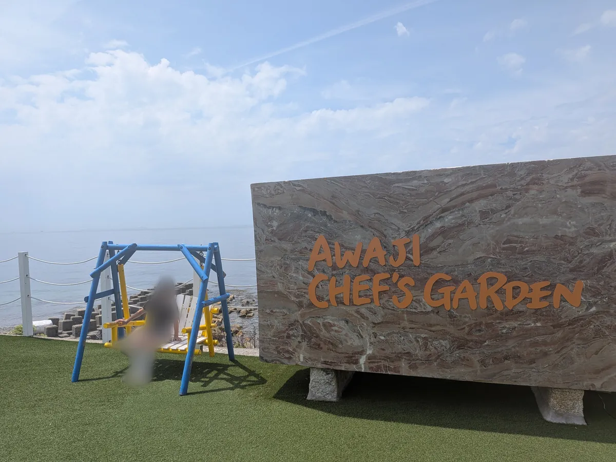 海沿いに立つAWAJI CHEF'S GARDENの石看板と青いブランコ、淡路島の海