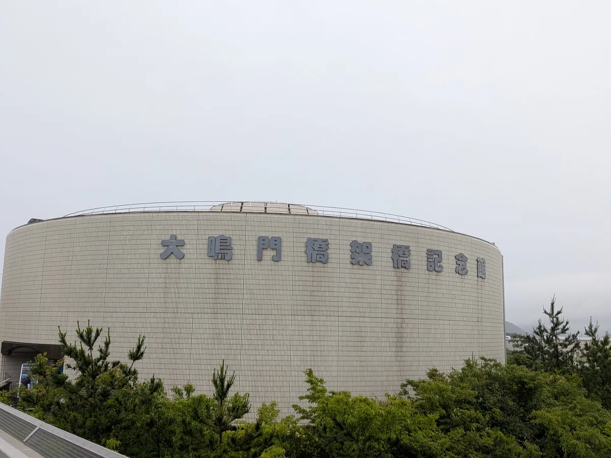 円形の大鳴門橋架橋記念館エディの外観。「大鳴門橋架橋記念館」の文字と曇り空