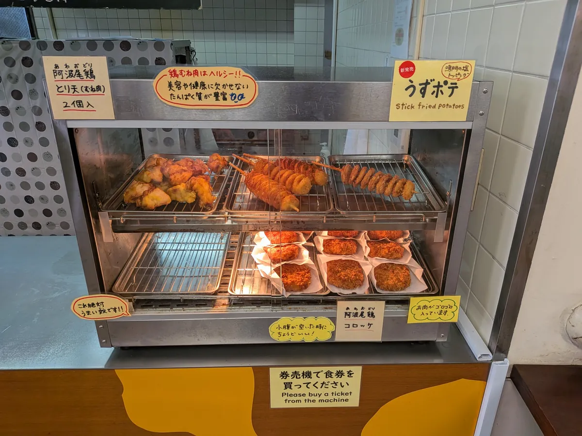 売店の揚げ物ケース。うずポテやコロッケ、阿波尾鶏のとり天が並ぶ
