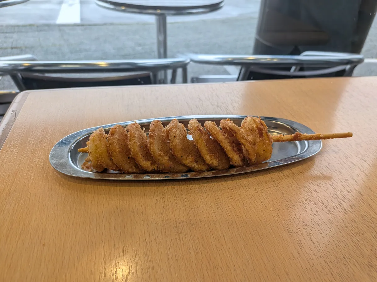 うずポテ。渦巻き状に串へ巻いたスパイラルポテトフライをステンレス皿にのせた様子