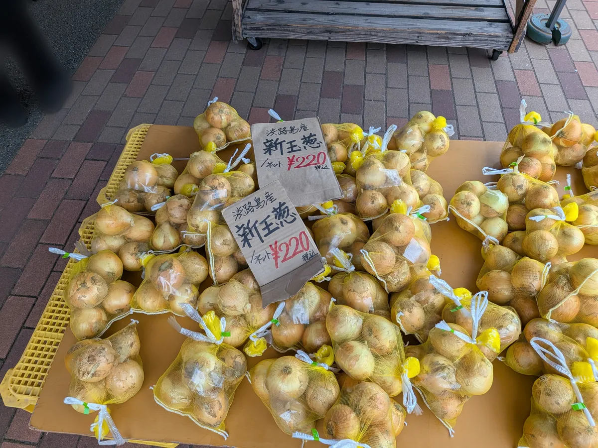 屋外売り場に並ぶ新玉ねぎのネット袋の山。手書きの値札