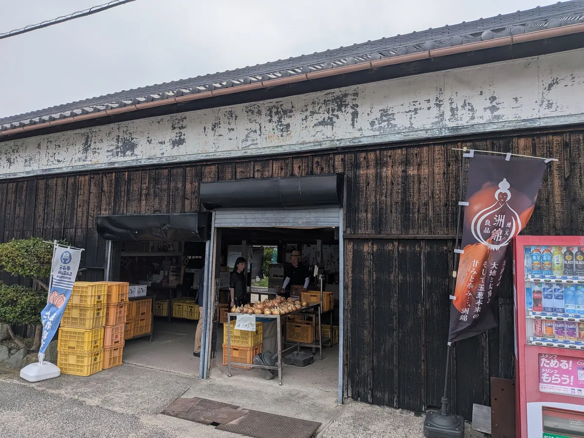 洲本農園の軒先の販売スペース。玉ねぎが並び、奥に人物(モザイク処理済み)