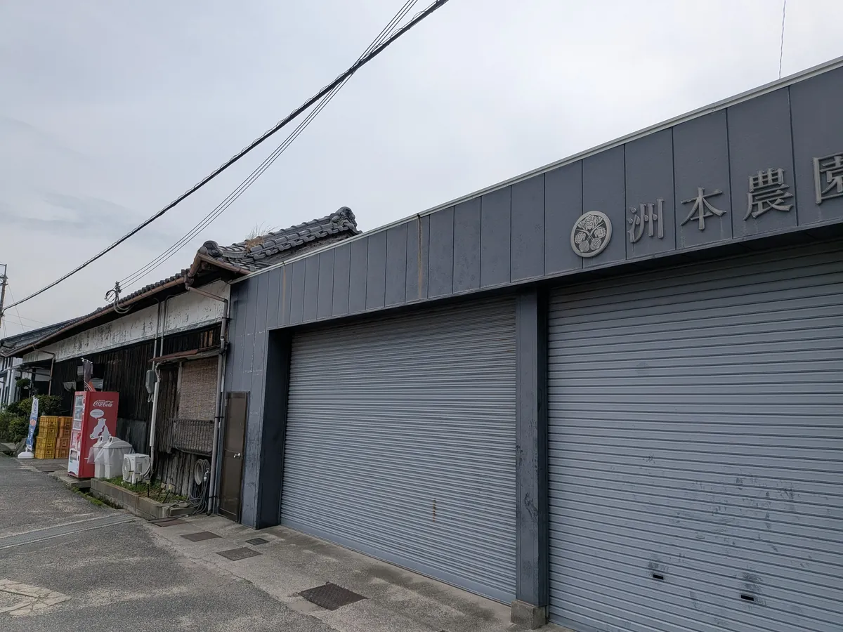 洲本農園の外観。瓦屋根の建物のシャッターに家紋と「洲本農園」の文字