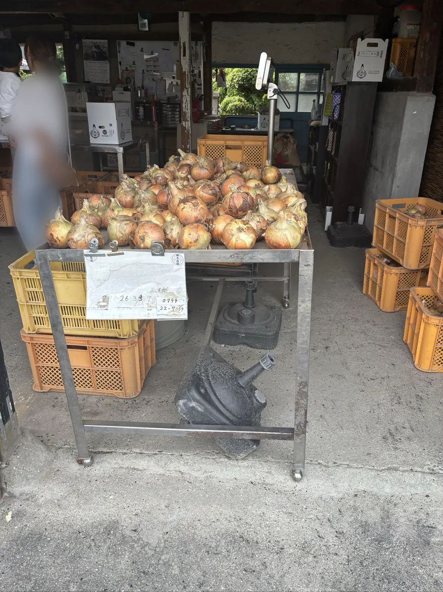 農園の売り場の台に積まれた淡路島産の玉ねぎ(左端の人物はモザイク処理済み)