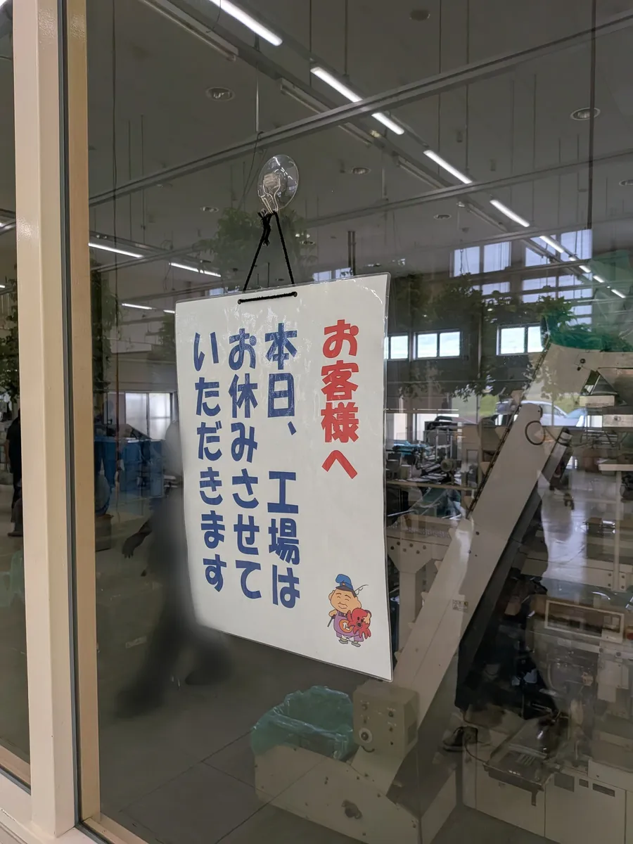 ガラス越しの工場ラインに掲げられた『本日、工場はお休みさせていただきます』の掲示