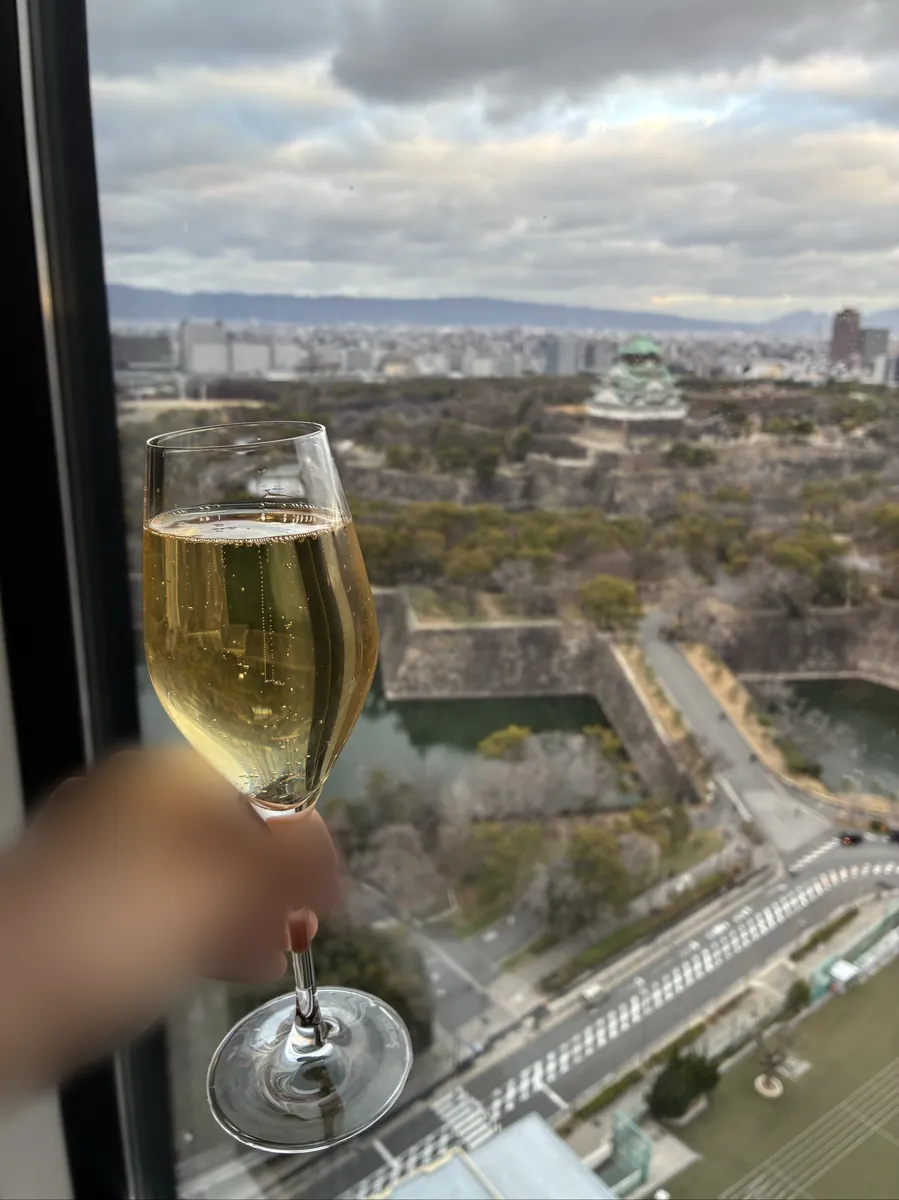 大阪城を背景に窓際で掲げたスパークリングワインのグラス