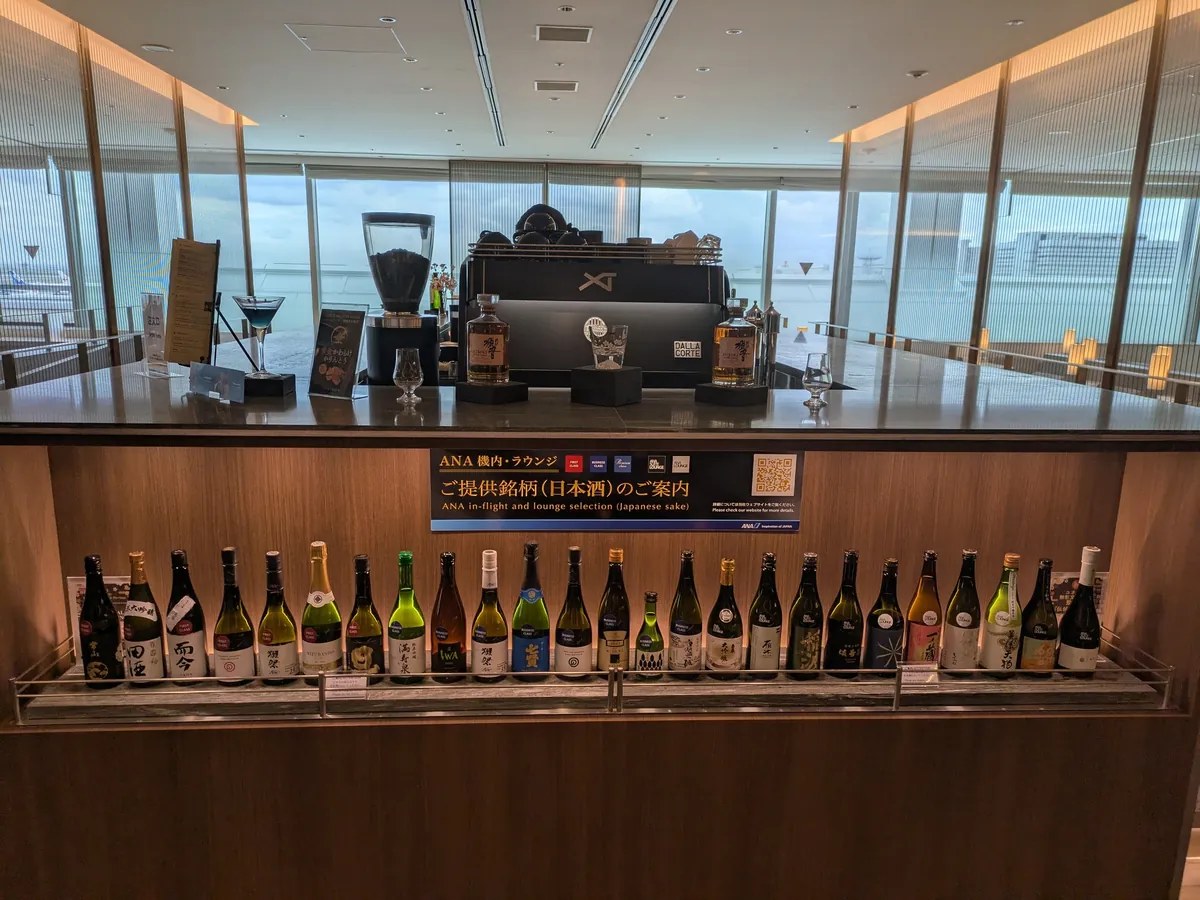 ANAスイートラウンジのバーカウンター。日本酒約20銘柄、響などのウイスキー、エスプレッソマシンが並び窓の外は滑走路。