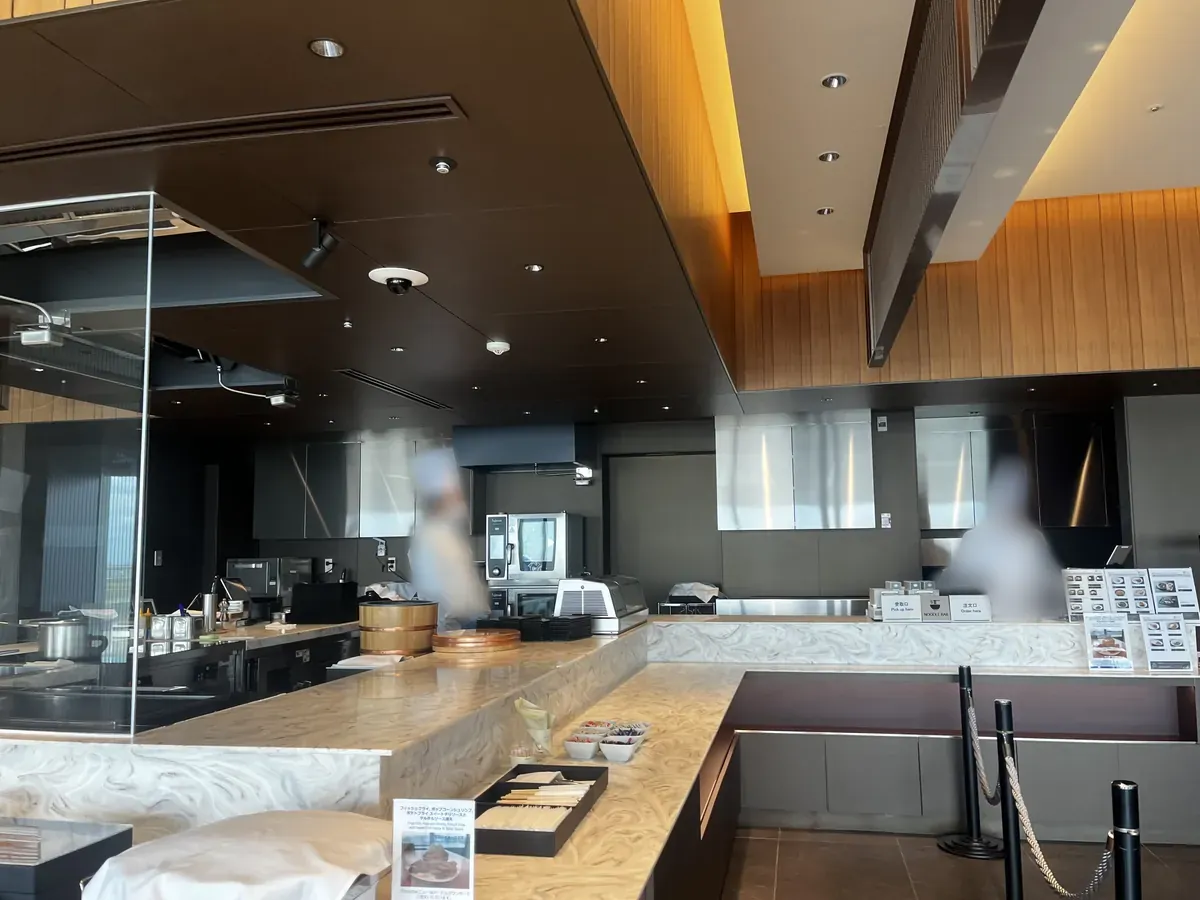 SUITE DININGのヌードルバー兼受け取りカウンター。ガラス越しの厨房と受取口(Pick up)の案内、メニューが並ぶ。