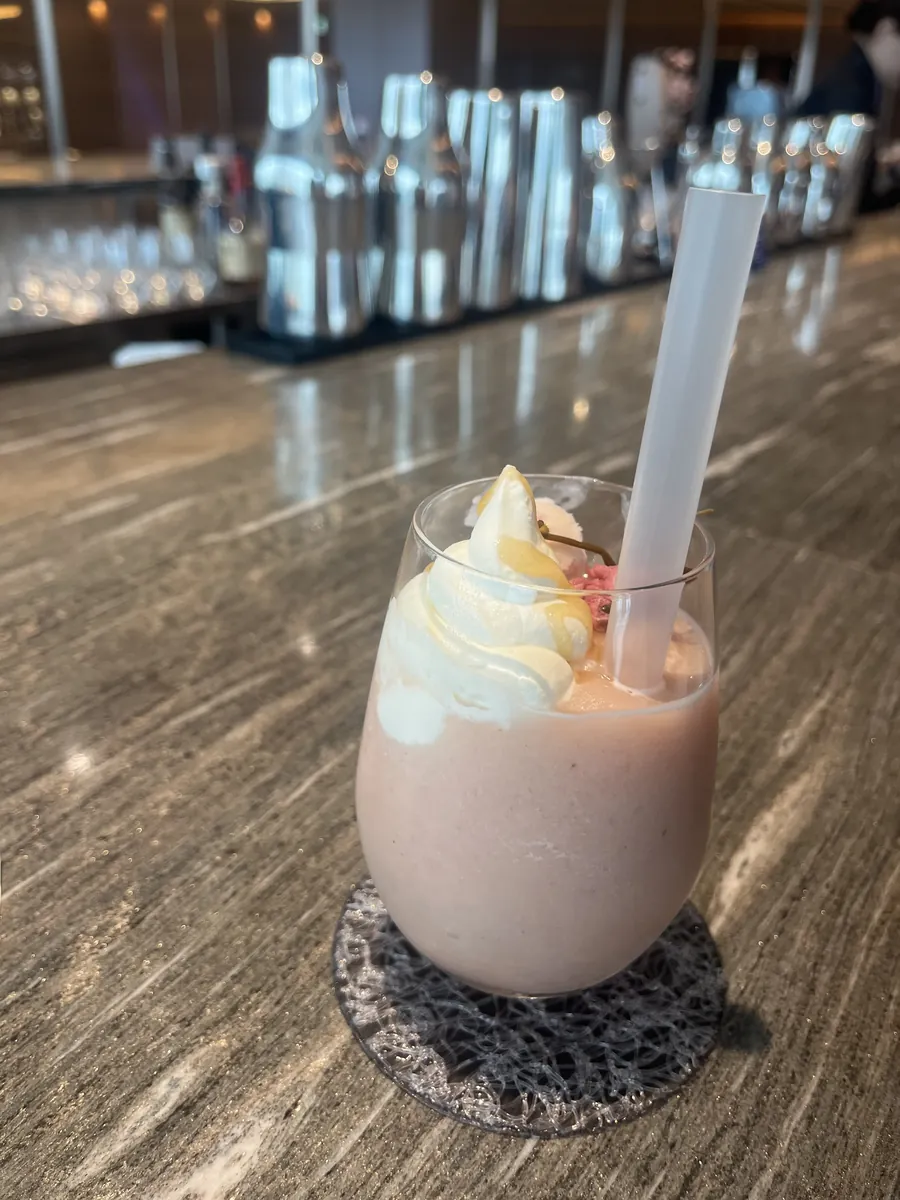 桜色のフローズンモクテルにクリームがのったANA Ice Magic。奥にバーのシェイカーが並ぶ。