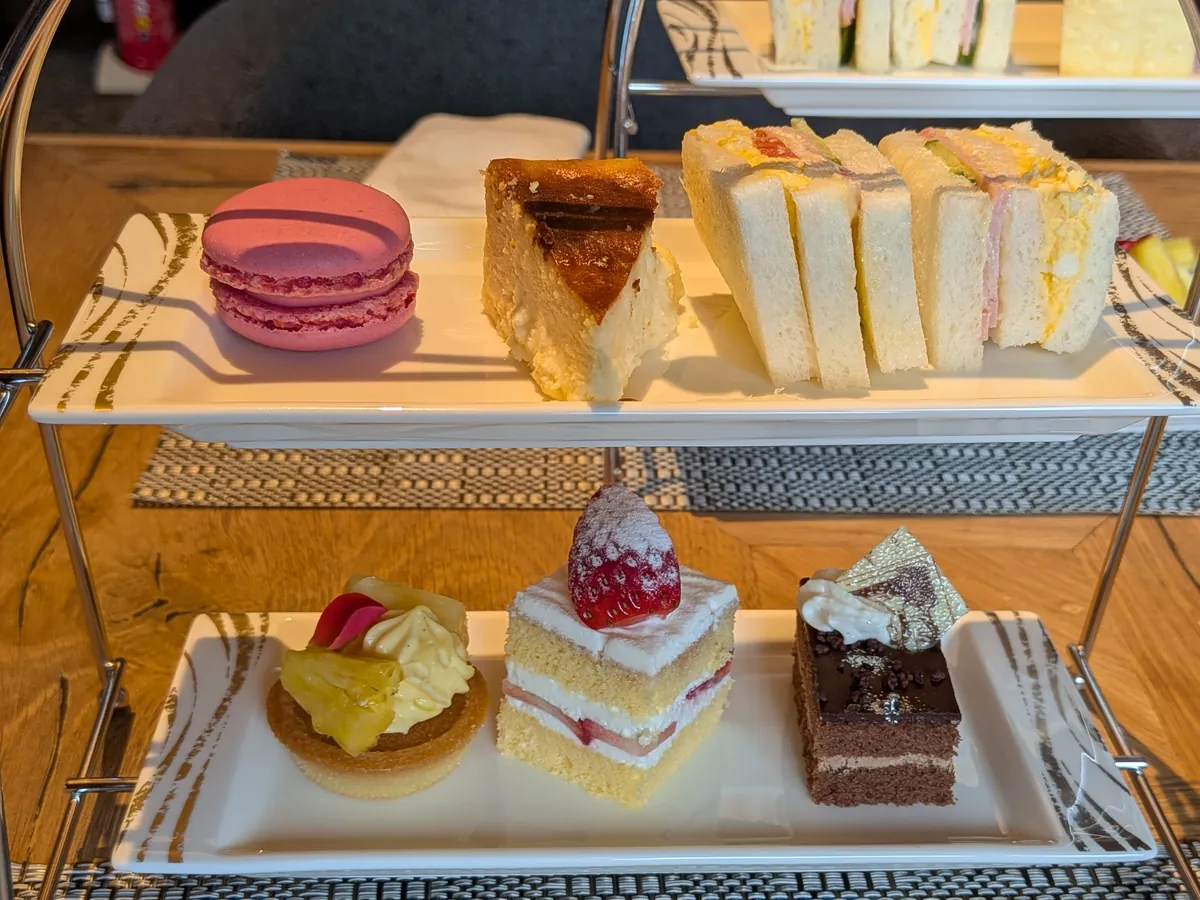 アフタヌーンティースタンドのアップ。ラズベリーマカロン、チーズケーキ、たまご・ハムのサンドイッチ、いちごショートケーキ、チョコレートケーキ