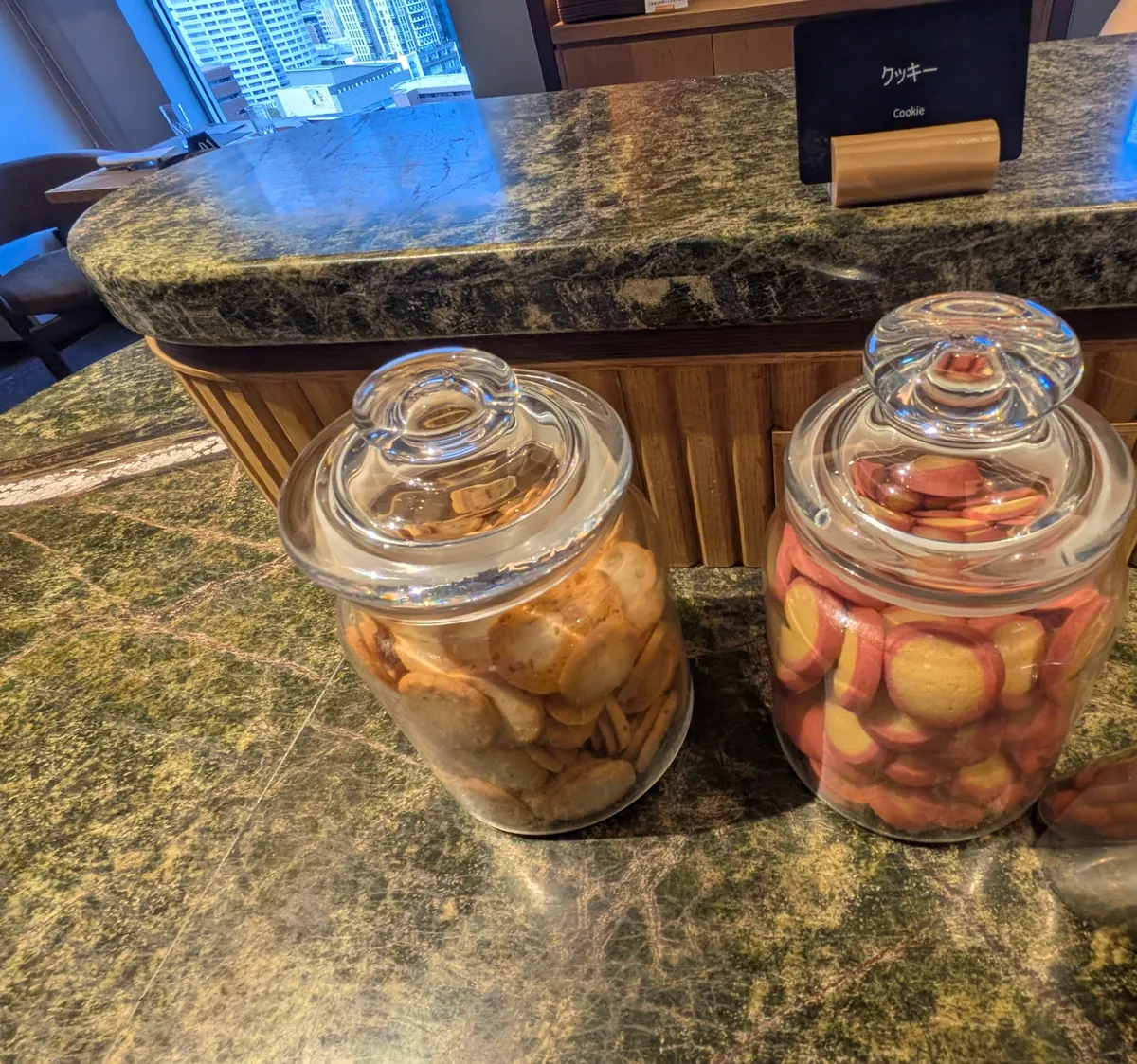 ビュッフェのクッキー。2つのガラス瓶に入った素朴なクッキーと、窓の外の街ビュー