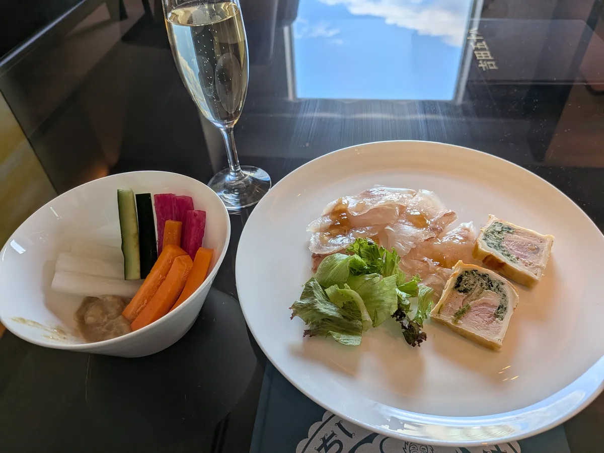 取り分けたカクテルタイムのおつまみ。カルパッチョとテリーヌの一皿に、スパークリングのグラスと野菜スティック(バーニャカウダ)
