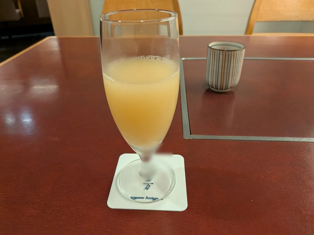 なだ万の和朝食のウェルカムドリンク。すっきりとやさしい甘さのリンゴジュースと湯呑みのお茶、なだ万のコースター