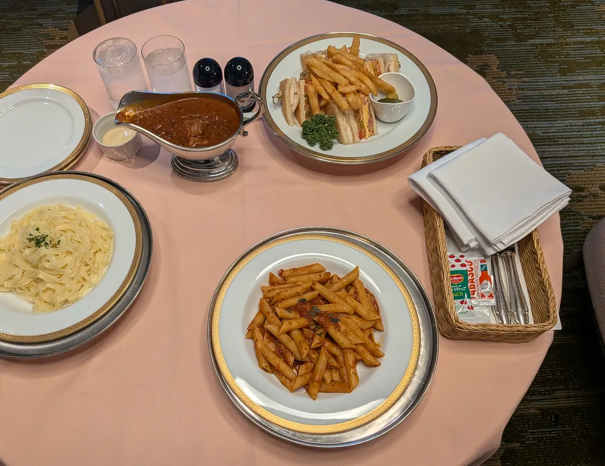 リーガロイヤルホテル大阪のルームサービスの洋食3皿。クラブハウスサンド、ペンネアラビアータ、タリアテッレとミートソースの銀のソースボート、ピンクのテーブルクロスにゴールド縁の食器