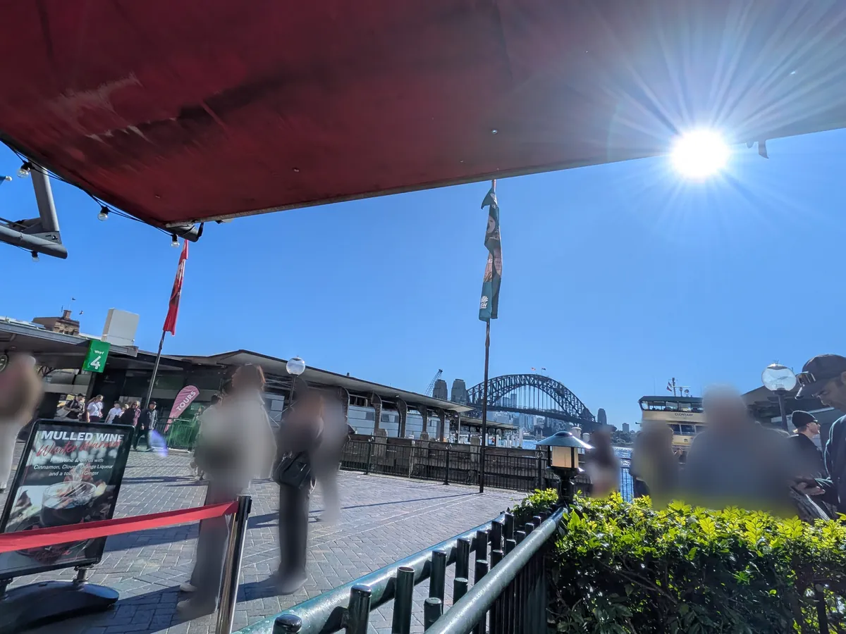 サーキュラーキーのテラス席の赤い日除けと、その先のWharf 4の表示とハーバーブリッジ