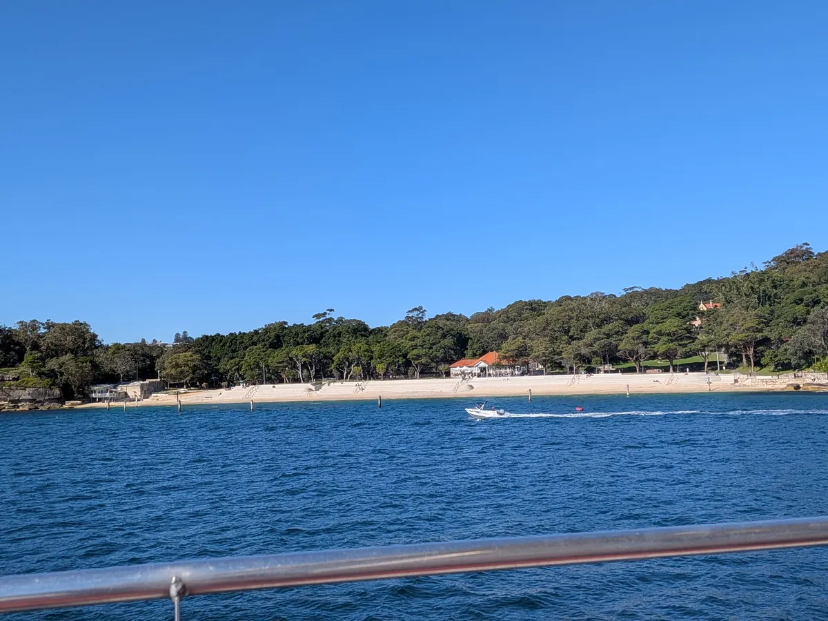 船から見た砂浜と緑の岬。穏やかな湾に小型ボートが浮かぶ