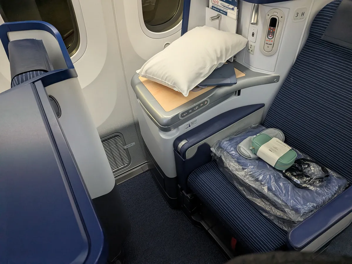 ANA B787国際線ビジネスクラスの座席。木目調テーブル・大型モニター・枕とアメニティが置かれた窓側席
