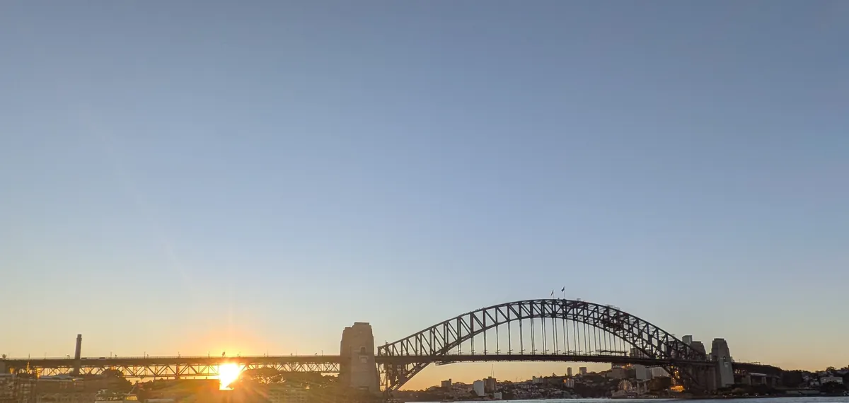 ハーバーブリッジの横に沈む夕日と、水面に伸びる金色の反射