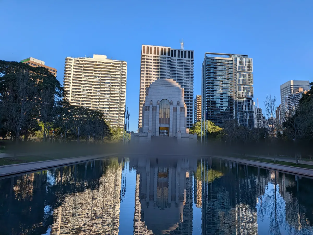 追憶の池の水面にアンザック・メモリアルの建物が映り込む。背後にシドニーの高層ビル群
