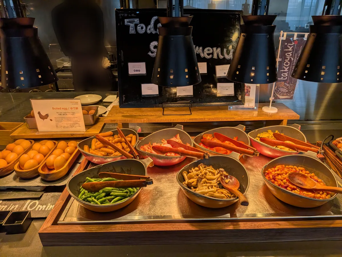 朝食のホットミールコーナー。ソーセージやベーコン、温野菜が保温皿に並ぶ