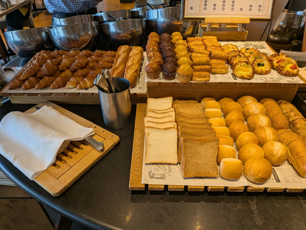 朝食のベーカリーコーナー。クロワッサンやロールパン、食パンが木のトレーに並ぶ