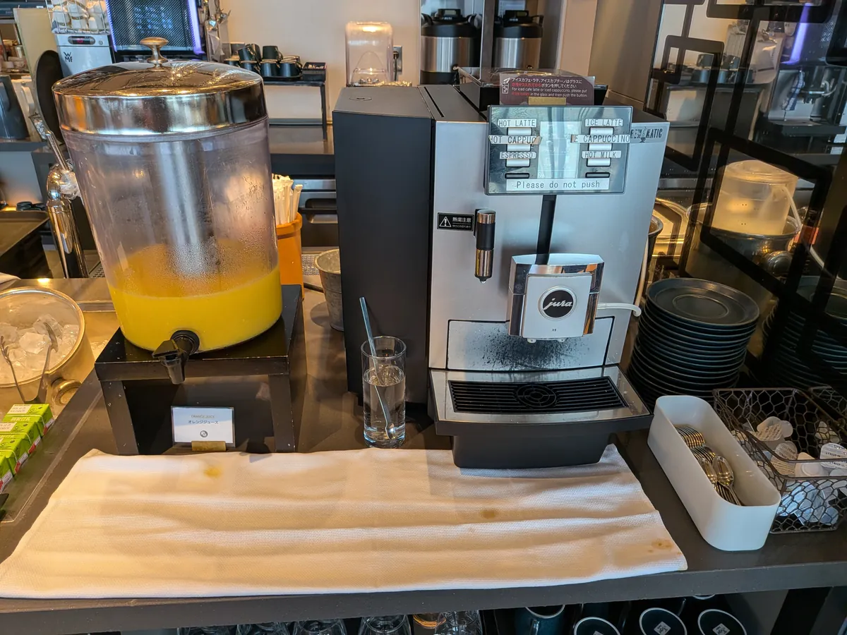朝食のコーヒーマシンとオレンジジュースサーバーが並ぶドリンクコーナー