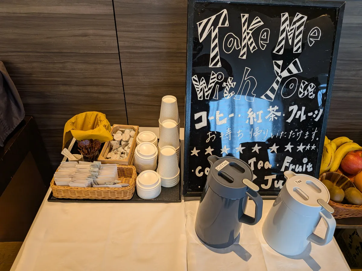 テイクアウト用コーヒーコーナー。黒板の案内と紙カップ、ポットが並ぶ