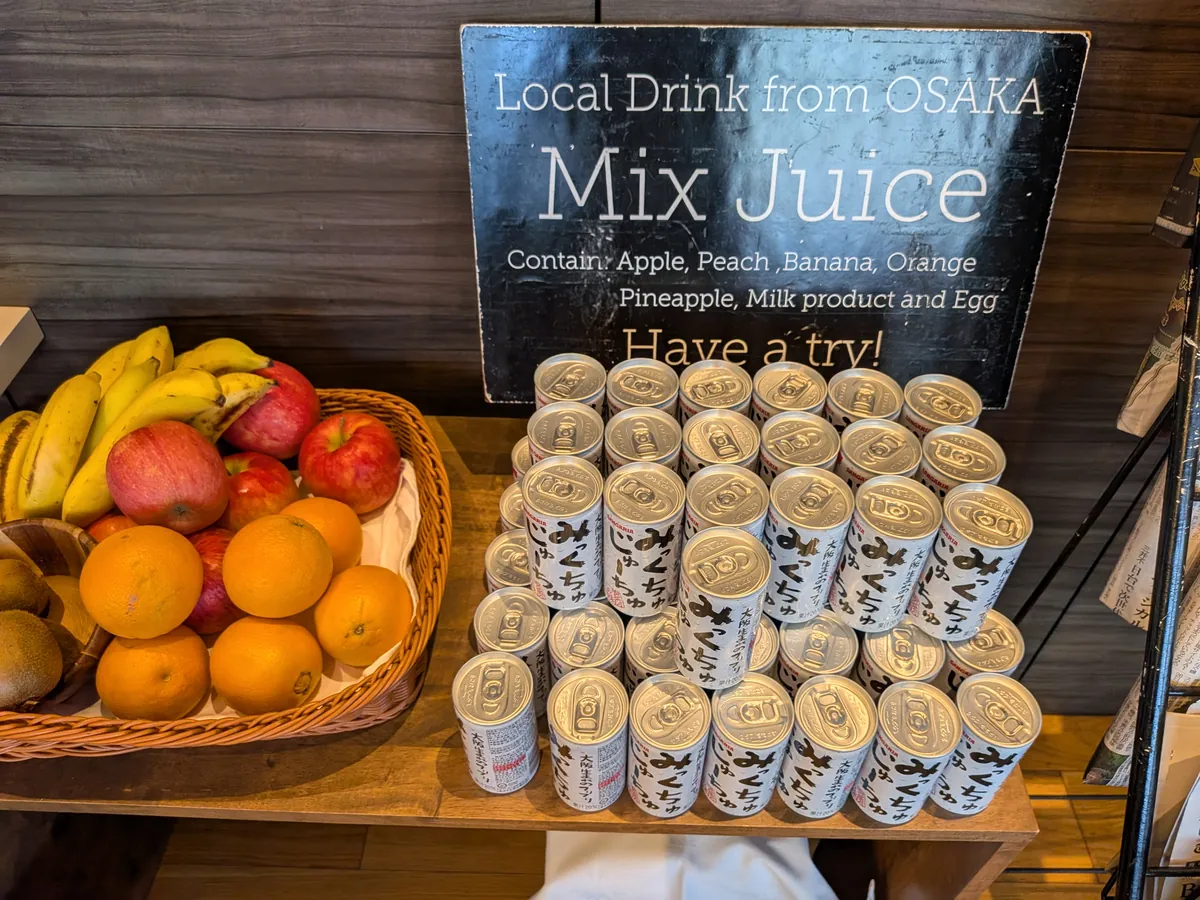大阪名物のミックスジュース「みっくちゅじゅーちゅ」の缶とフルーツのかご、Local Drink from OSAKAの看板