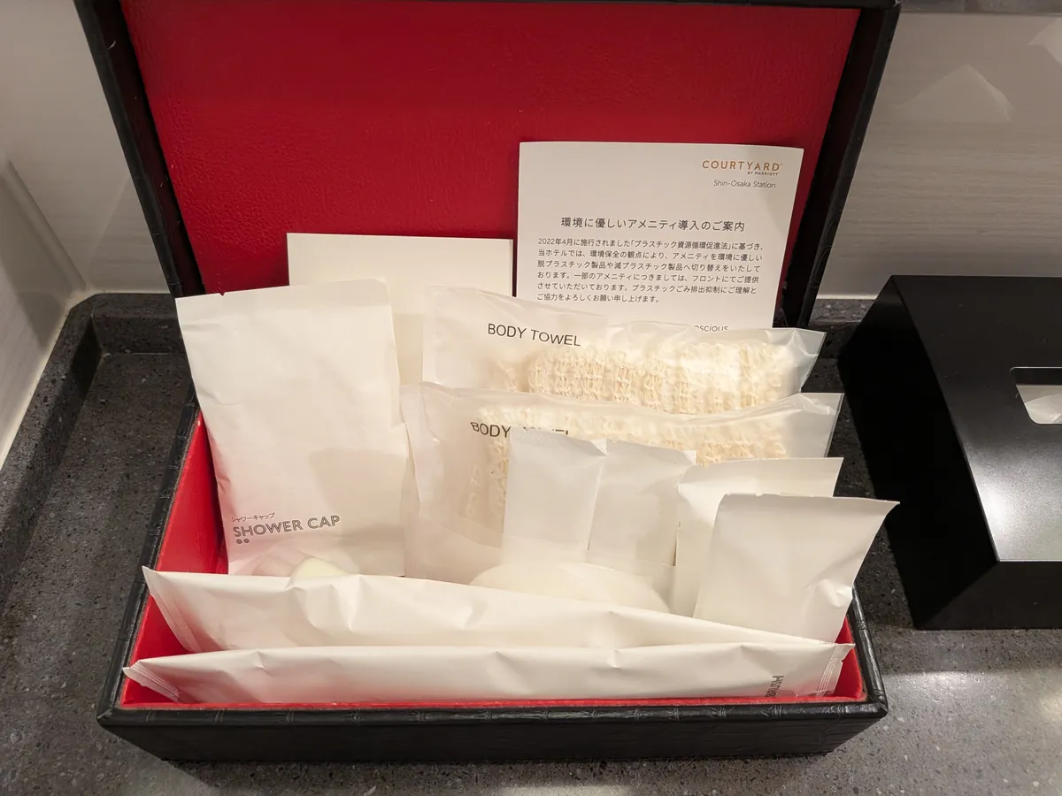 赤い内張りのトレーにまとめられたタオル類とシャワーキャップ、ボディタオル