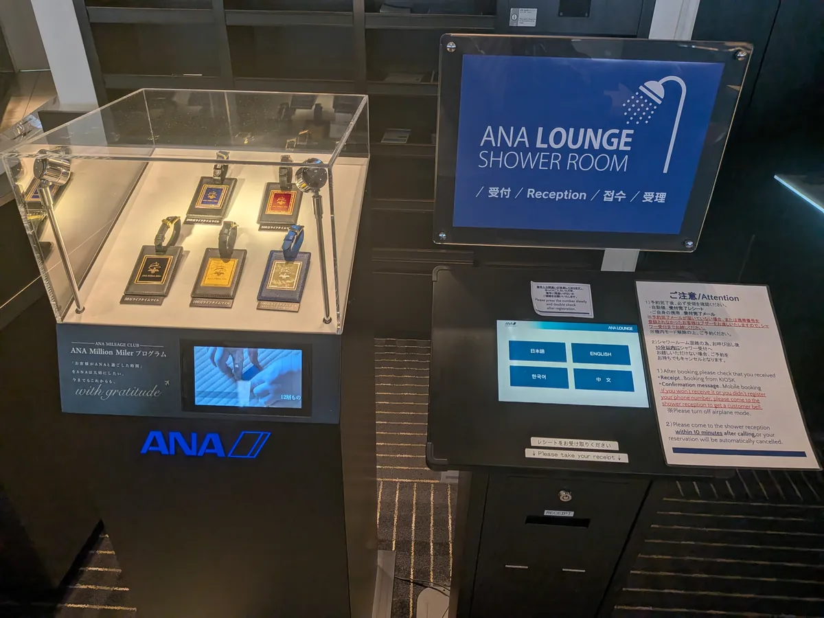 ANA LOUNGEのシャワールーム受付と、ANA Million Miler Programの記念ラゲッジタグが展示されたコーナー。