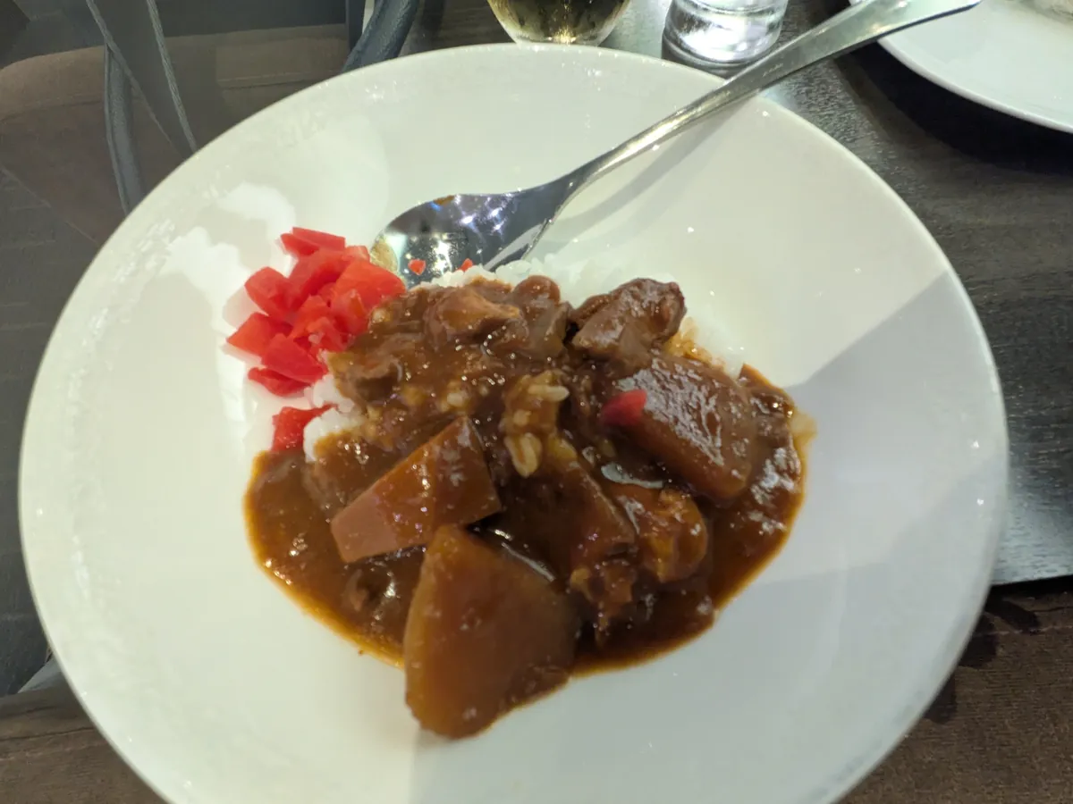 ラウンジで提供された、具材がゴロゴロ入ったカレーライスと福神漬けが盛り付けられた白い皿。